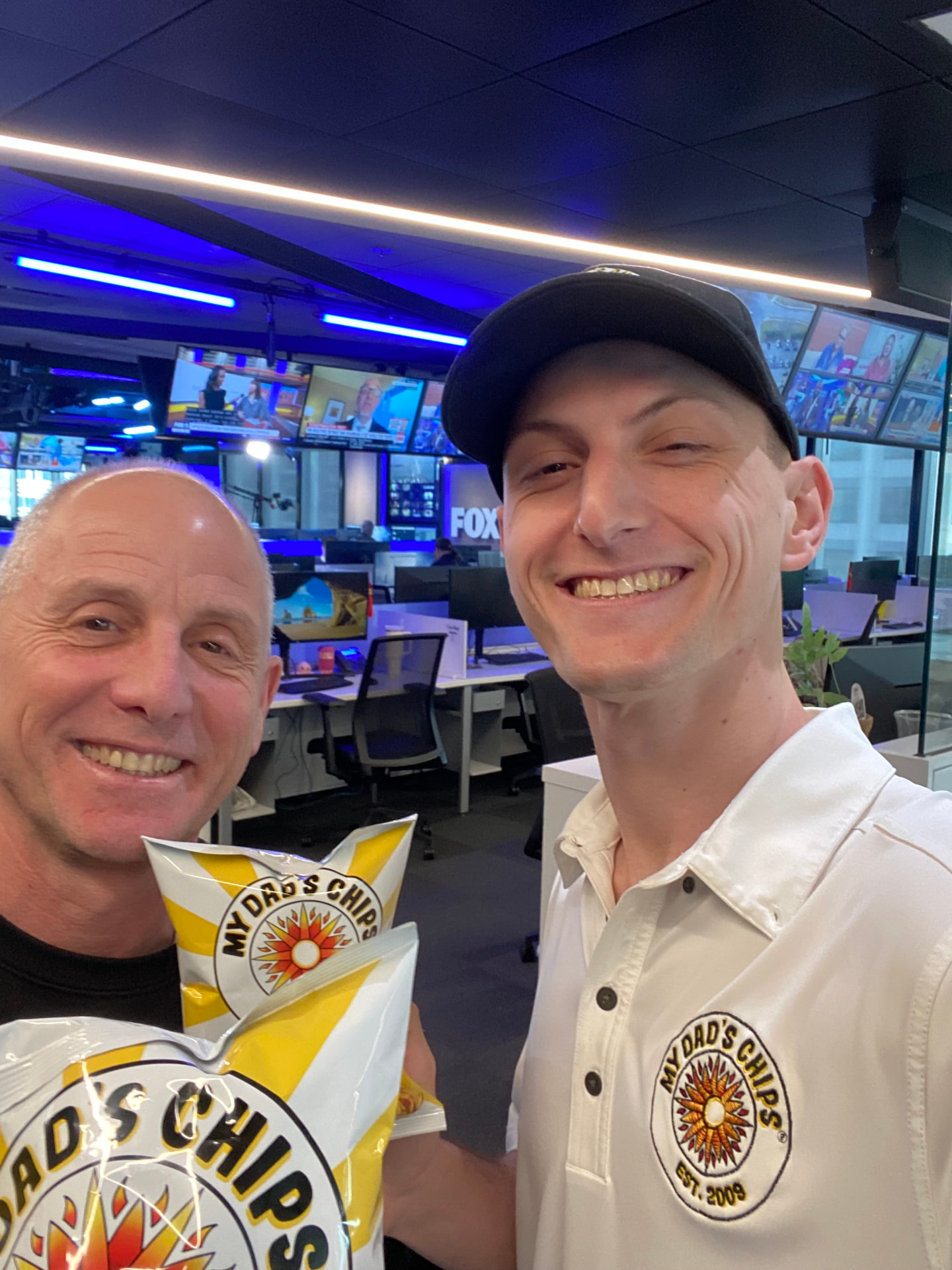 Gary and Brian holding bags of My Dad's Chips in a newsroom studio.