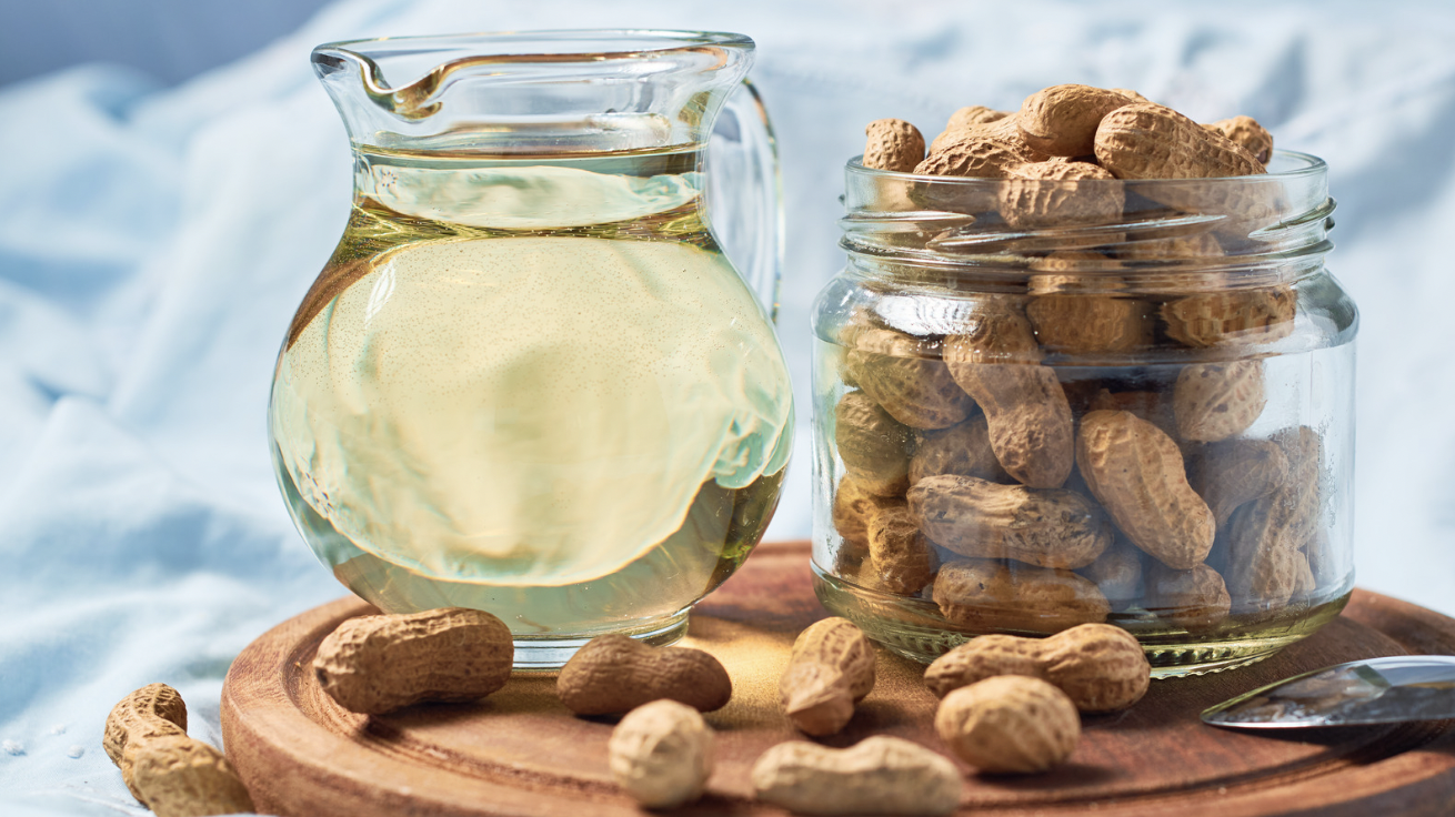 Glass pitcher of peanut oil beside a jar of peanuts